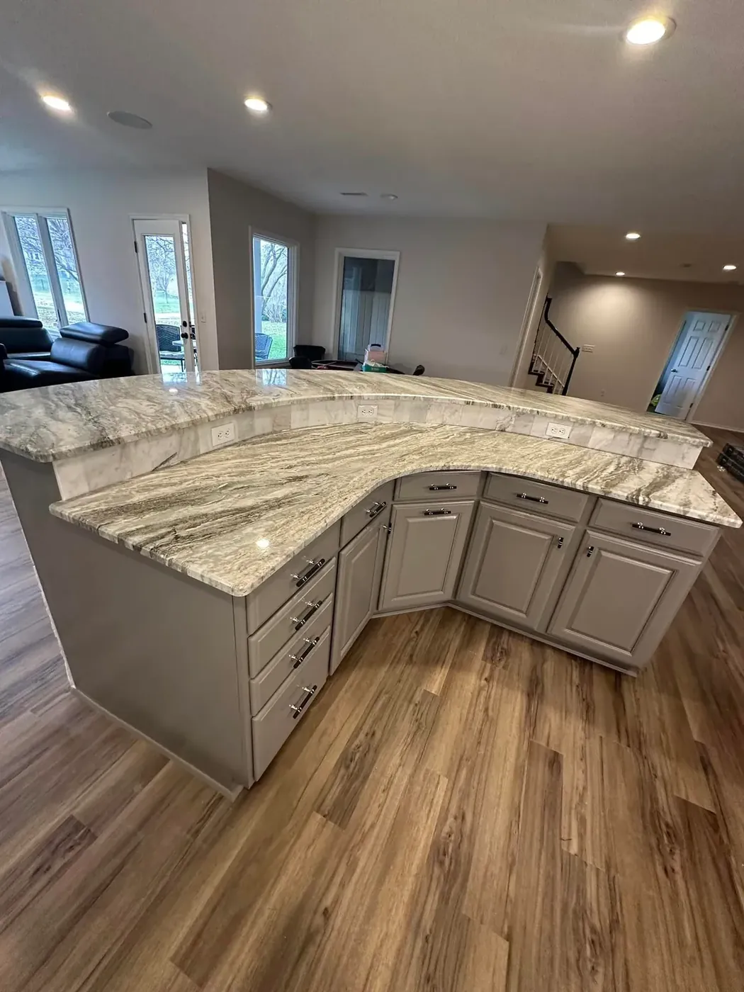 Curved granite kitchen counter over gray cabinets and plank flooring