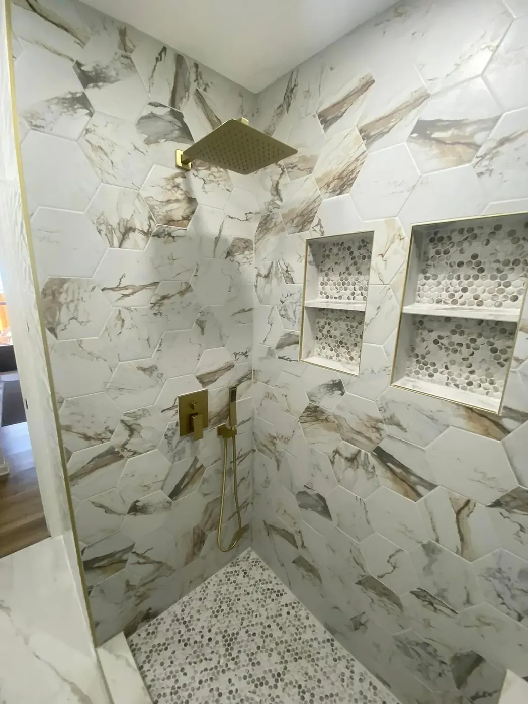 Walk-in shower tiled in marble pattern with niches and gold fixtures