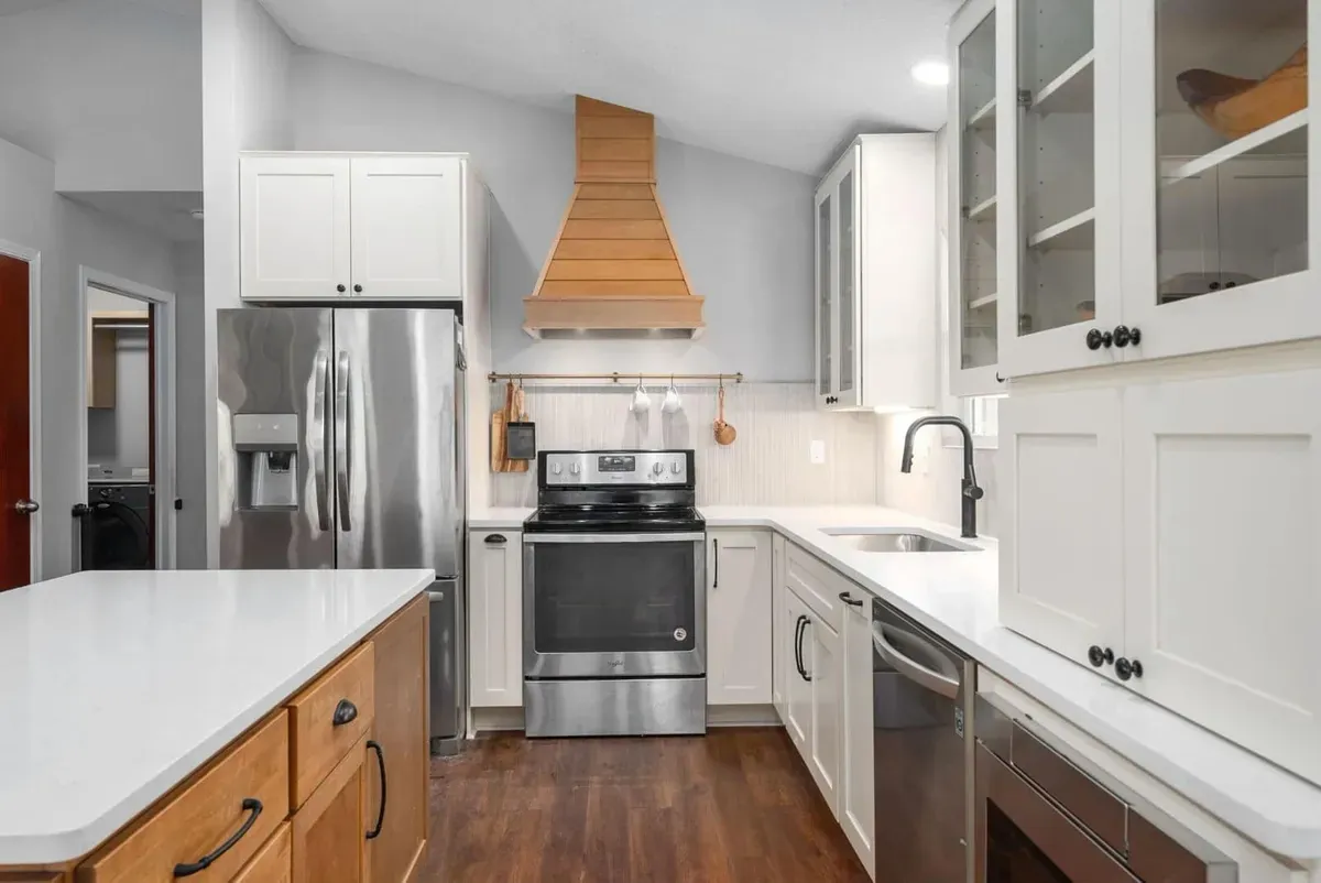 White kitchen with stainless appliances and a wood range hood